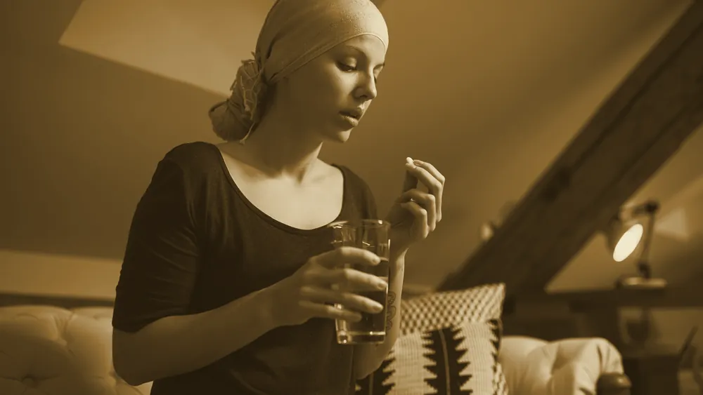 A young woman with cancer holding a pill and a glass of water
