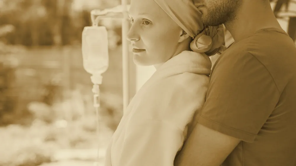 A loving partner embracing a woman ill with cancer near a window