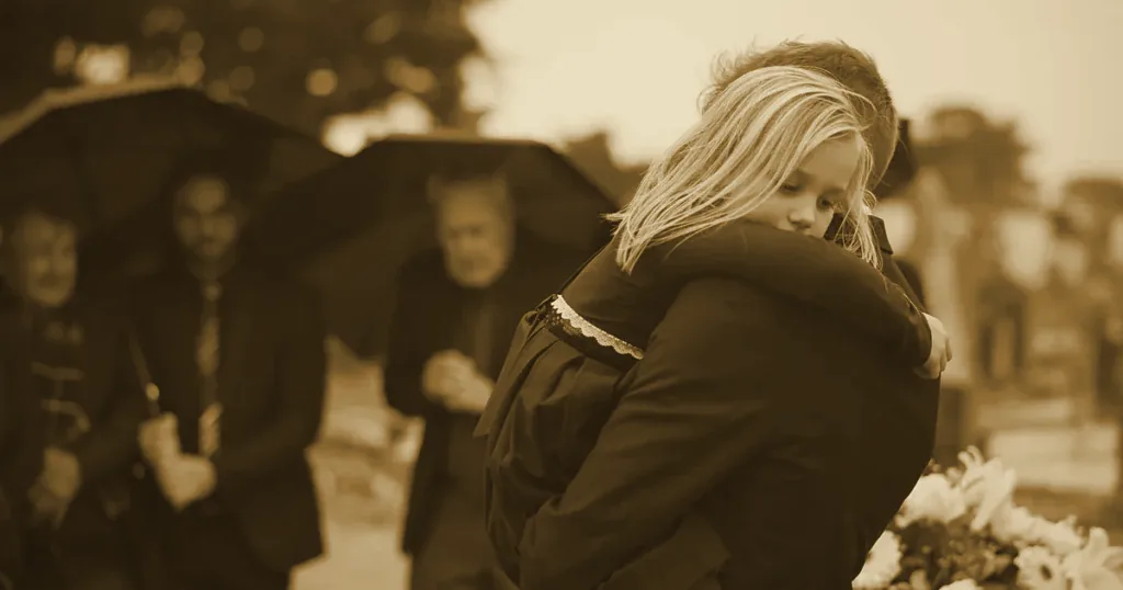 A grieving father embracing a child at a funeral