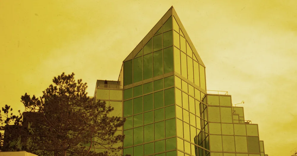 A modern green-glass government office tower framed by trees against a golden Nova Scotia sky