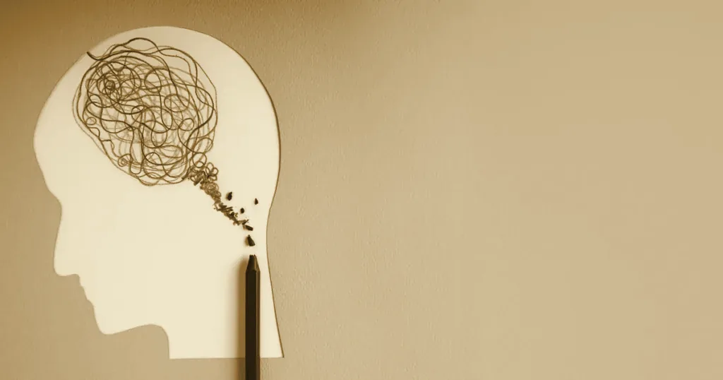 Paper cut-out of a head with tangled lines and a broken pencil, a mental-health concept